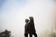 couple standing on a foggy mountaintop back to back 