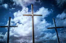three crosses in front of clouds in a blue sky 