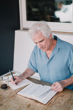a man writing in a journal and reading a bIble 