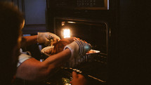 man pulling a thanksgiving turkey out of the oven 