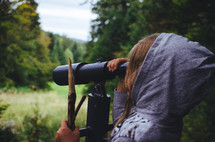 a girl looks through a telescope into a forest