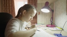 Education concept. Cute smart school child girl writing doing homework sit at home table. Teen girl doing school assignment. Happy child studying at home in the evening.
