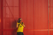 African-American woman taking a picture with a camera standing in front of a red wall 