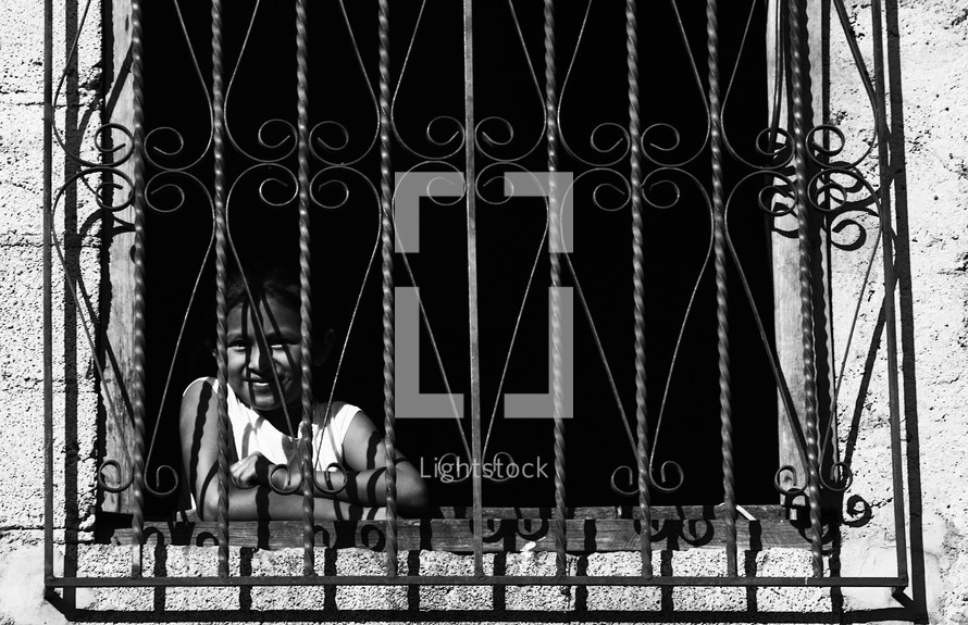 A girl smiling from behind a window with bars