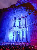 Large group of people sitting on the ground at night, the rock cut architecture of Al Khazneh or The Treasury at Petra, Jordan.