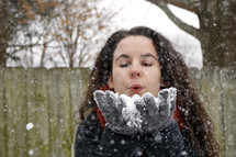 a woman blowing snow from cupped hands 
