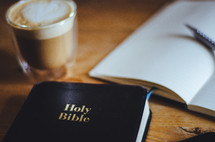 A bible, coffee and open notebook on a table
