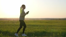 Fitness athlete in sportswear during outdoor running session. A young woman runner is listening to music in earphones and training in summer. Concept of workouts running and healthy lifestyle.