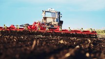 Red combine harvester plows the loose earth in field for planting new wheat on sunny summer day. Large plot farmland. Agricultural equipment for technical works. Production large volume of products.