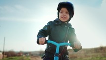 Cute little boy child wearing safety helmet learning to ride first balance bike in sunny day. Happy boy riding bike, having fun outdoors on sunset time. Active sport family concept. Slow motion 120fps