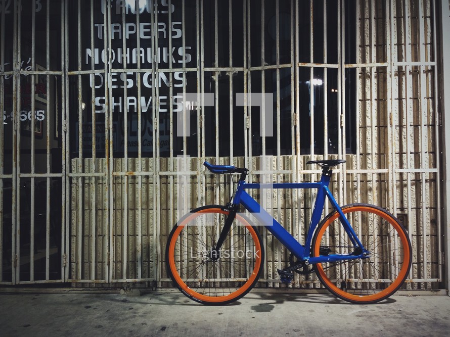 A bike resting in front of a gated store front. 