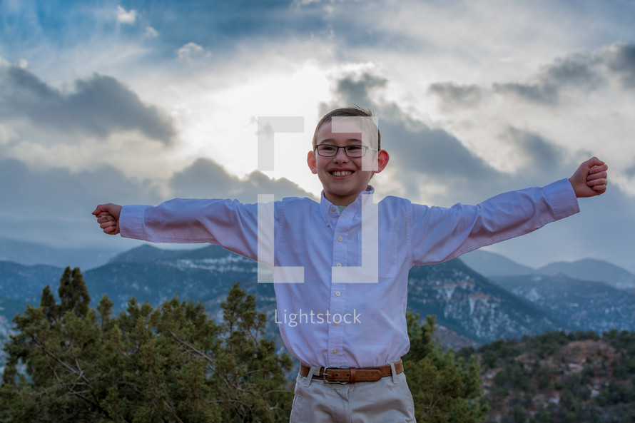 boy child with open arms with mountains behind him 