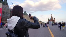 Tourist woman on travel take a picture on smartphone of Red Square in Moscow. Young woman taking pictures of sights.