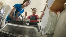 Young girls fill the dishwasher with dirty dishes