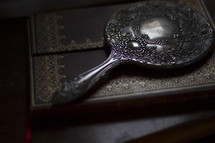 An antique, silver mirror laying on a book.