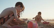 Three kids playing on the beach building sand castles together