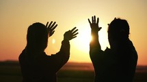 Silhouette of reaching, helping hand, hope and support each other over sunset. People hands reaches for the sky and closes the sun, the sun's rays pass through the hand. Religion concept footage.