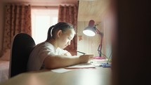 Education concept. Cute smart school child girl writing doing homework sit at home table. Teen girl doing school assignment. Happy child studying at home in the evening.