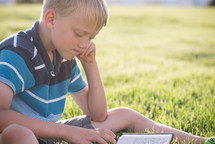 a child reading a Bible in the grass 