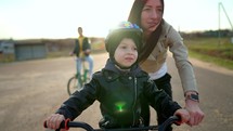 Childhood bike concept. Mother teaching son to ride bicycle. Young mom teaching son to ride bike first time on countryside rural road at sunset. Happy kids on bikes. The best moments together.