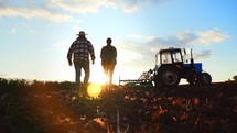 Silhouette couple walking through rural suburban area of field. Economic production with help of tractor machinery. Beautiful landscape nature. Suburban area with farm land. Healthy natural products.