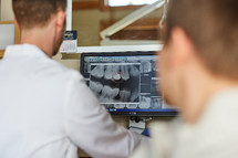 a dentist looking at X-rays of teeth and talking to his patient 