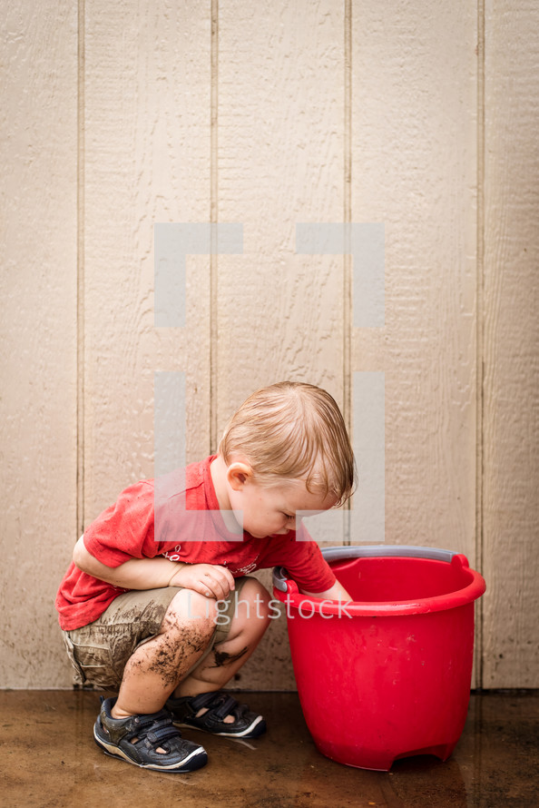 a toddler boy playing in a bucket of water 
