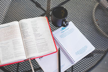 a opened Bible and cup on an outdoor table 
