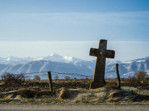 cross and fence in front of snow capped mountains 