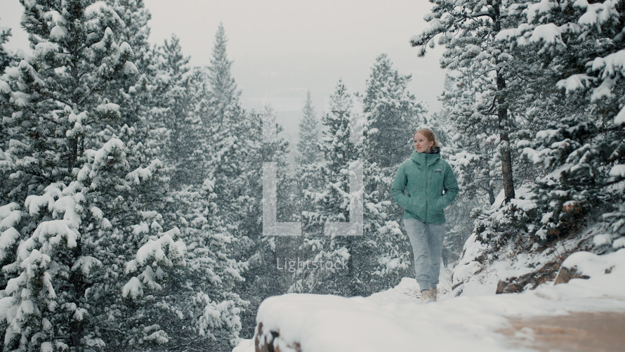 female hiker walks in the mountain woods as snow falls around her 
