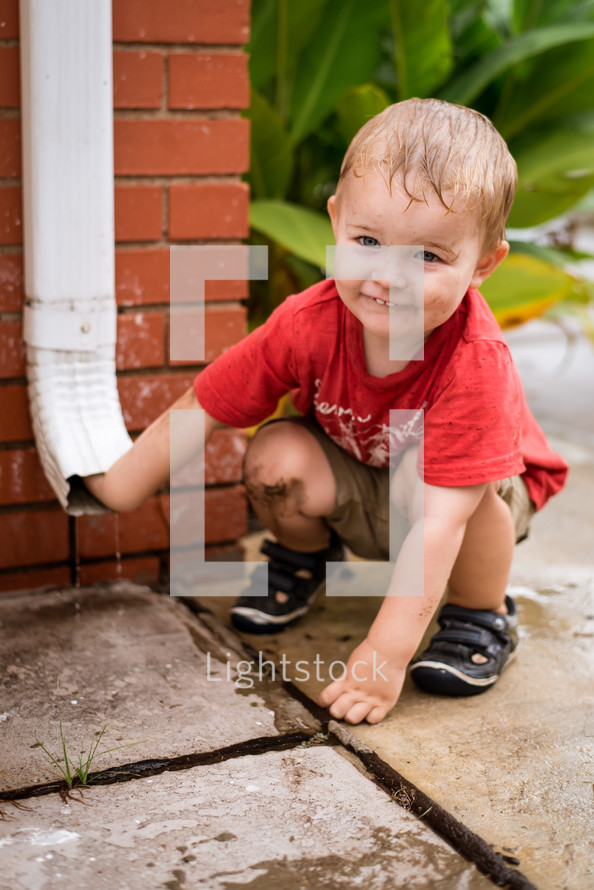 toddler boy playing with a rain spout 