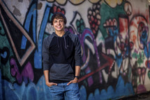 young man standing in front of a graffiti covered wall 