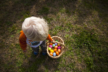 Child carrying a basket of Easter eggs while standing in the grass.