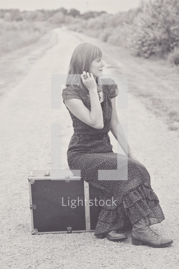 woman sitting on a suitcase on a dirt road 
