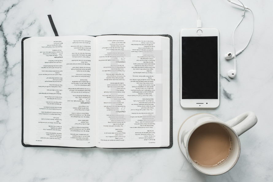 overhead view, coffee mug, smartphone, opened Bible, and earbuds on a table