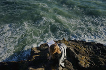 woman sitting on rocks along a shore writing in a journal 