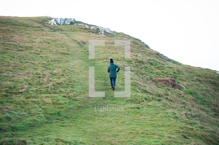 a woman walking up a green hill 