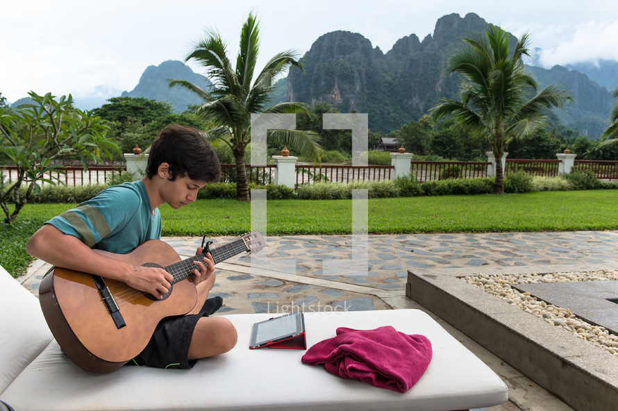 boy playing a guitar near palm trees 