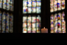 candle and a stained glass windows in a church 