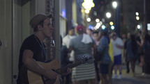 street performer playing a guitar on a crowded city sidewalk at night 