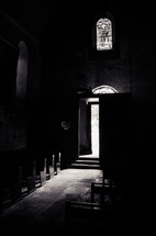 A b&w shot of the interior of an old stone church with wooden pews