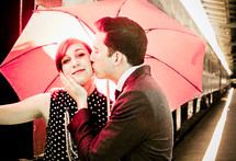 a couple kissing under a red umbrella near a train 