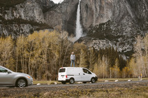 man standing on the roof of a van with a waterfall in the background in Yosemite 