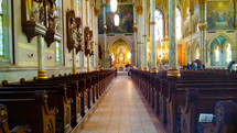 A historic church view of the center aisle and pews lined on each side of the aisle and walls adorned with stained glass windows, sculptures and three dimensional artwork dating back from the early 1800s. 