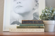 stacked old books, framed photo, and house plant on a table 