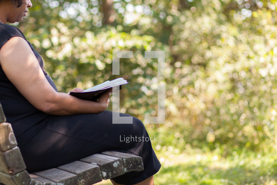 a woman sitting on a bench reading a Bible 