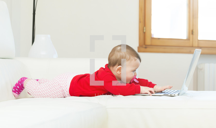 Eight months old baby girl using a laptop on the couch at home