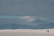 A couple treks through the dunes of White Sands National Monument, searching for a spot to rest. 