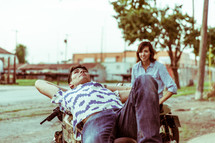 a man lying across a motorcycle talking to a woman 