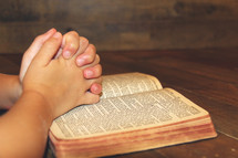 child's praying hands over a Bible 